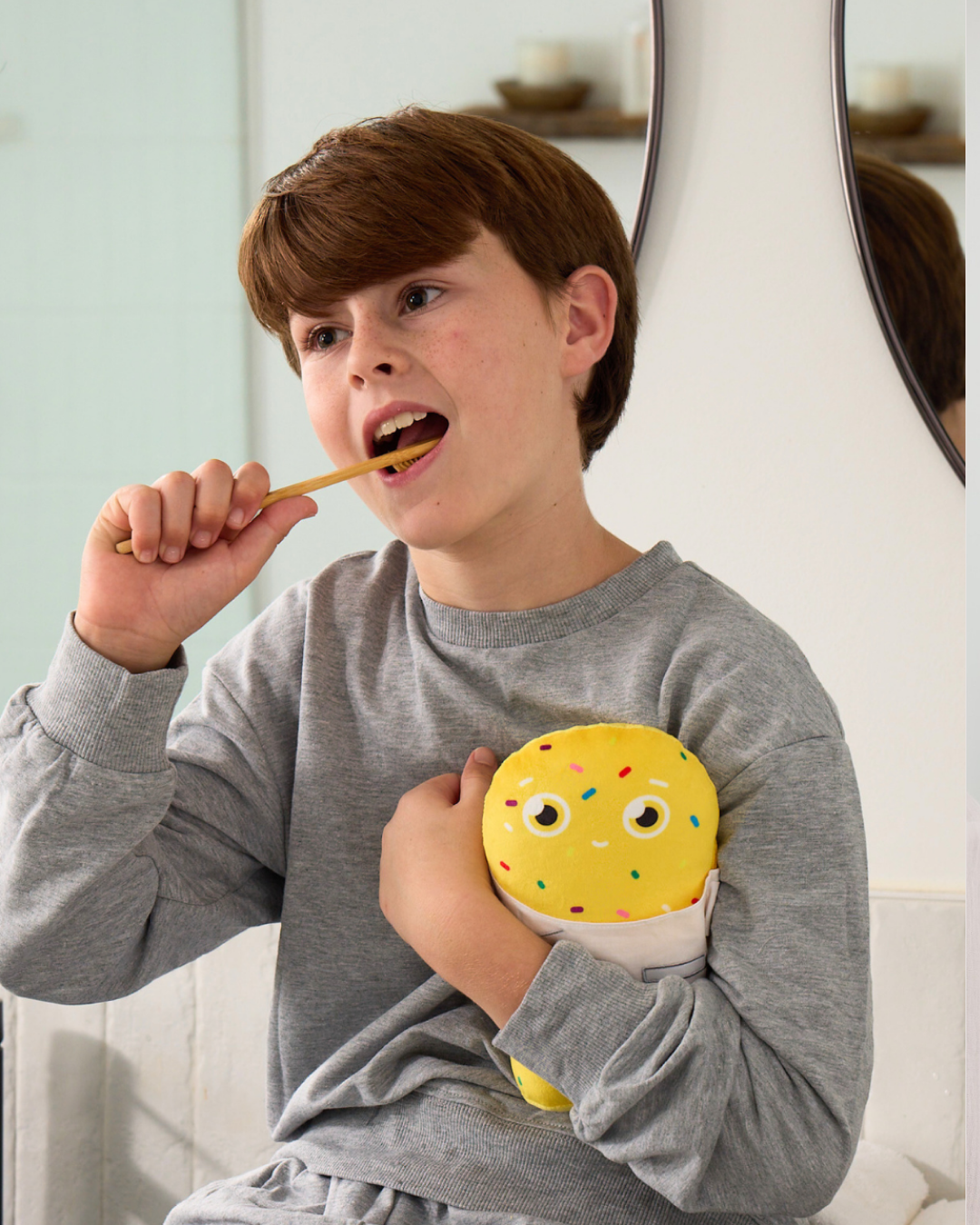 Child brushing teeth with a yellow toothbrush and holding a yellow plush RiseWell toy.