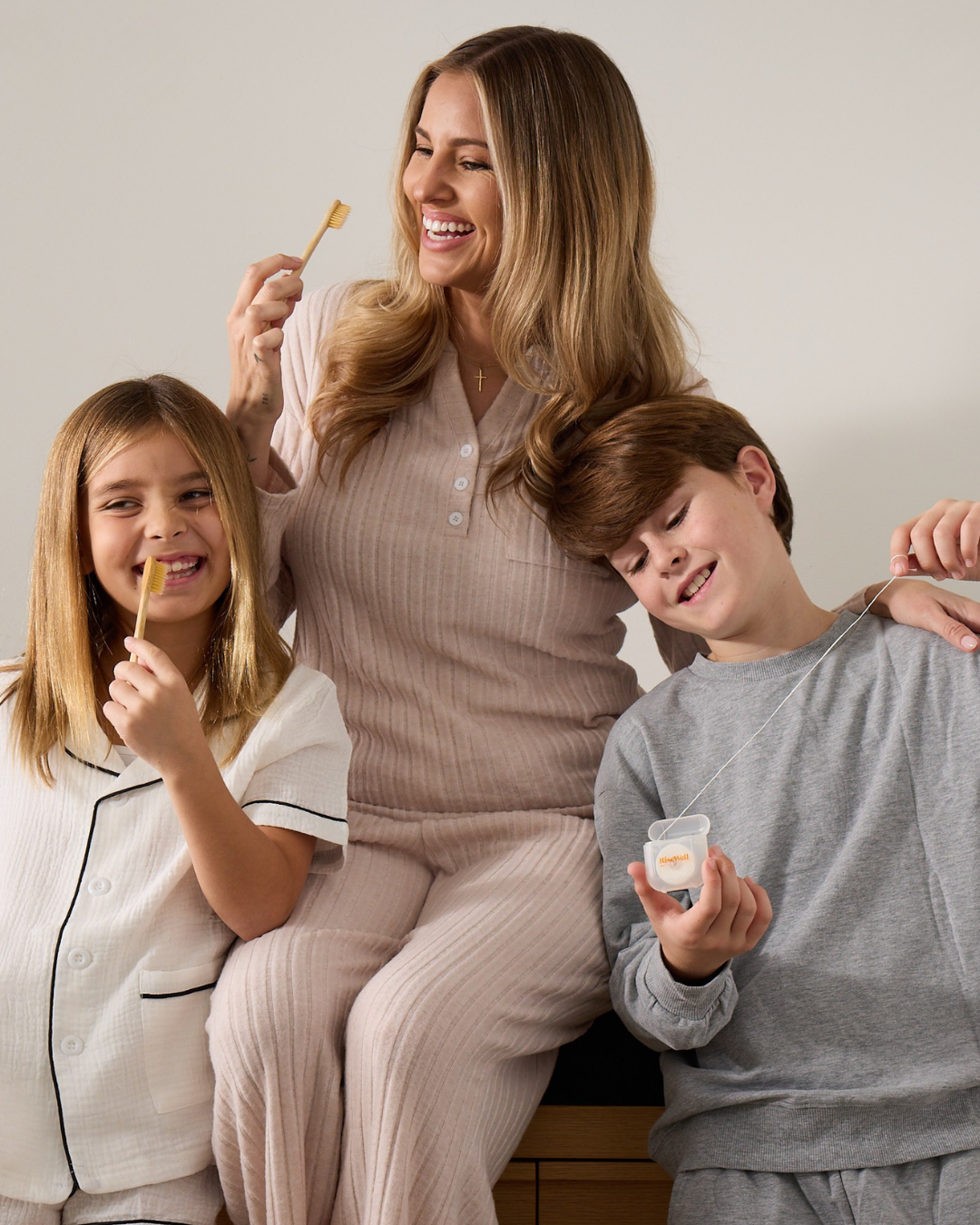 Woman and two children sitting together, with RiseWell toothbrushes and dental floss.