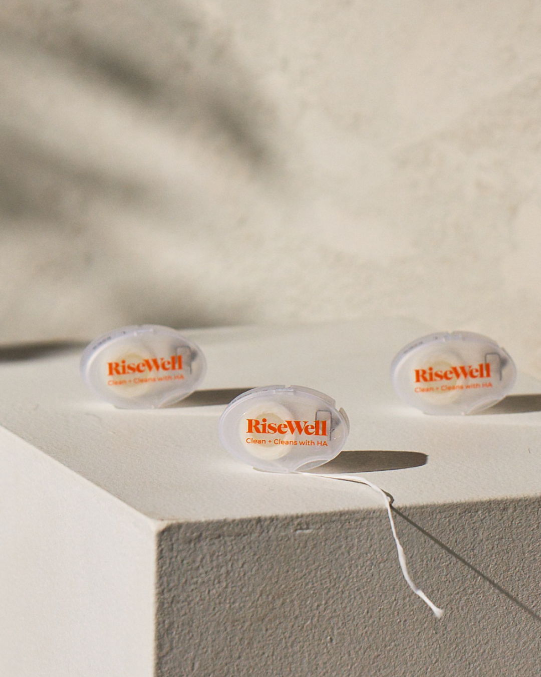 Three RiseWell travel floss cases on a light surface with a blurred background