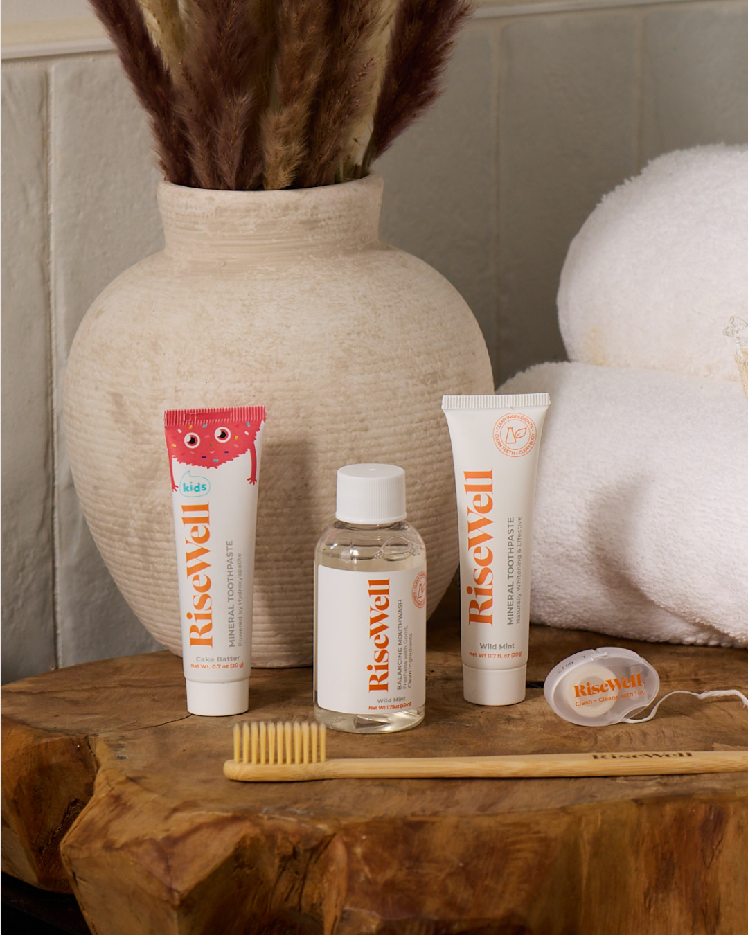 RiseWell skincare products on a wooden surface with a vase and towel in the background