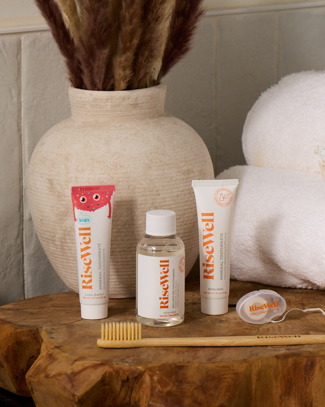 Risewell dental care products on a wooden surface with a vase and towel in the background.