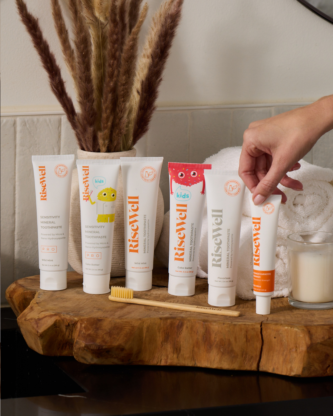 Collection of RiseWell products on a wooden surface with a hand reaching for one of the products.